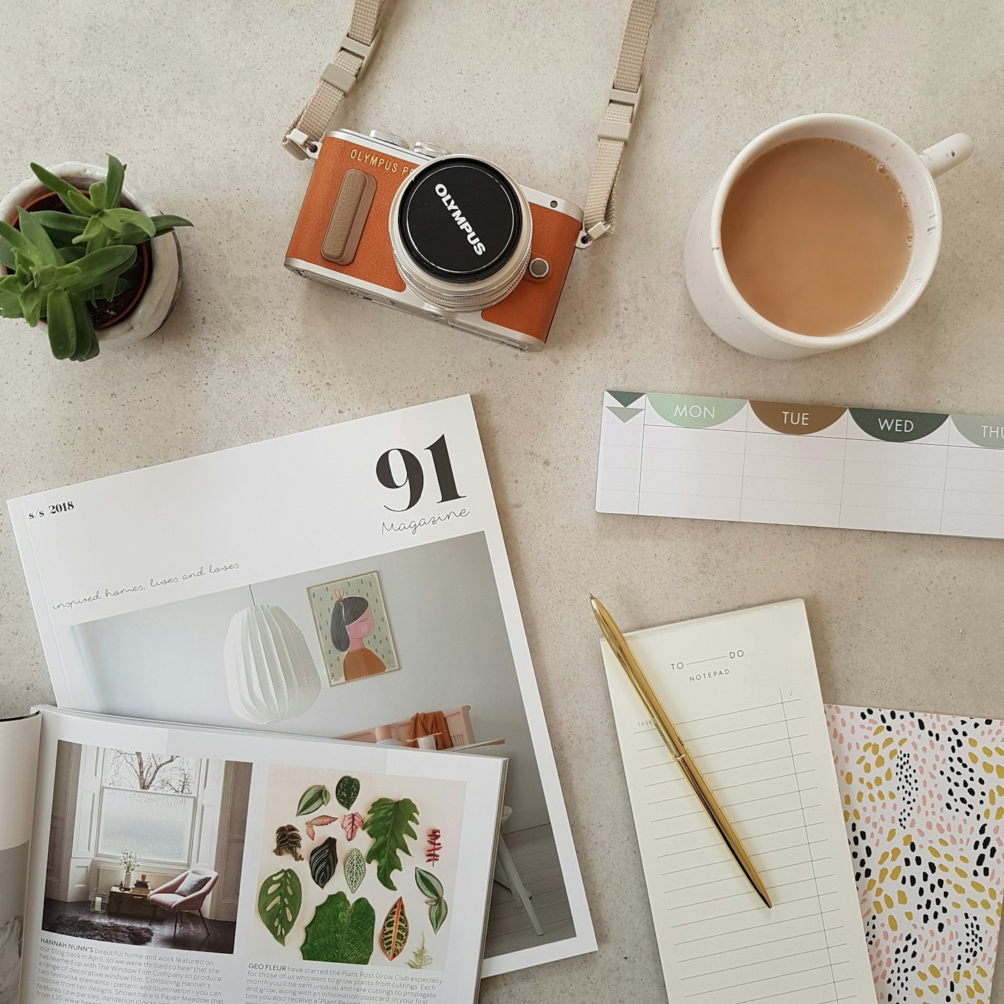 Desk flat lay with an open magazine, orange camera, and coffee.