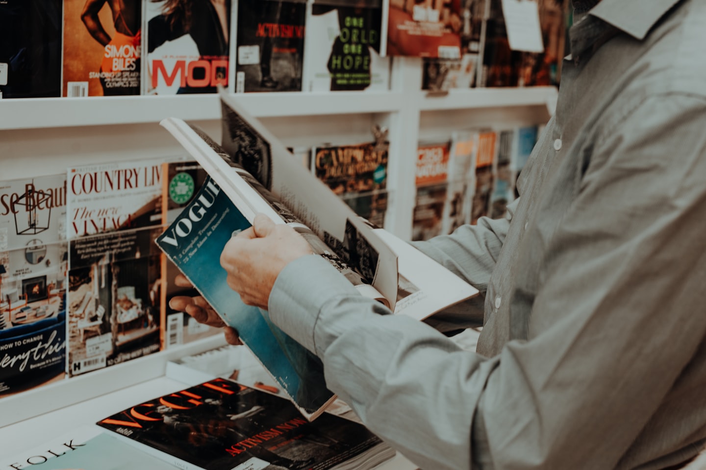Person's hands flipping through a VOGUE magazine at a newsstand.