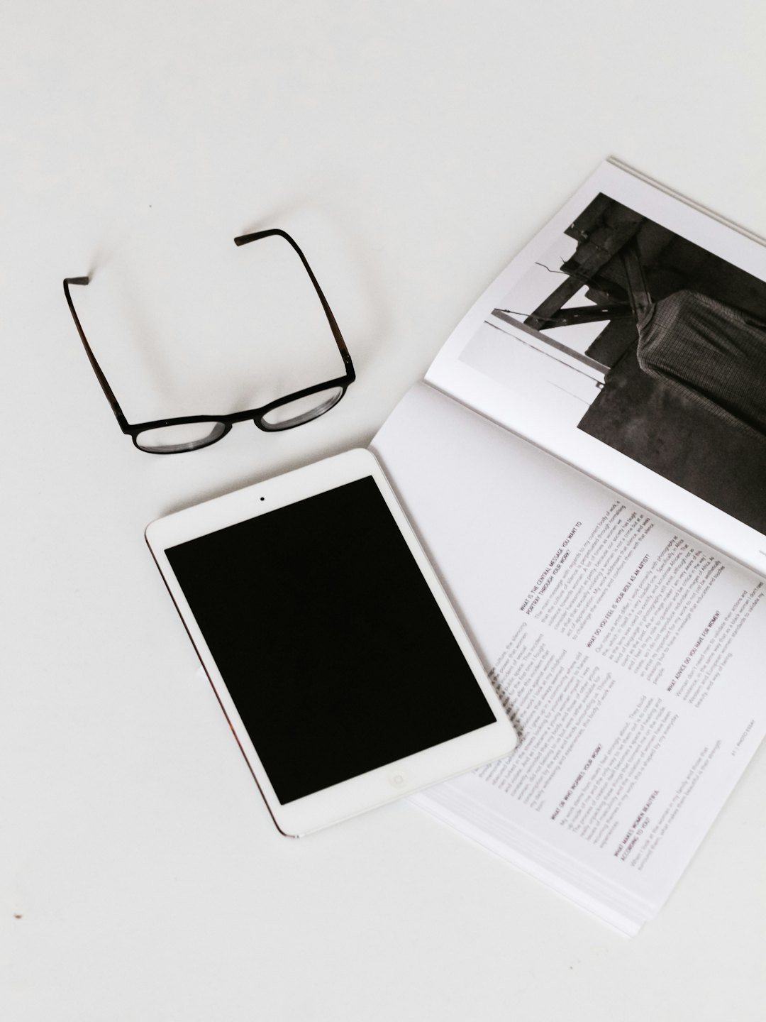 Reading glasses, tablet, and open magazine on a white desk.