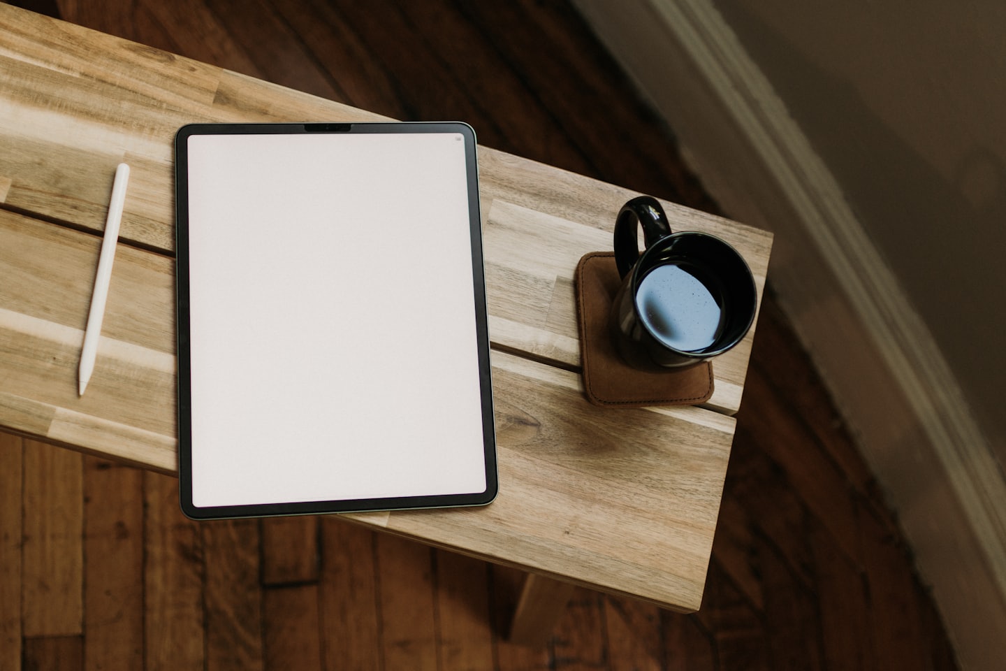 Tablet, stylus, and coffee on a wooden table.