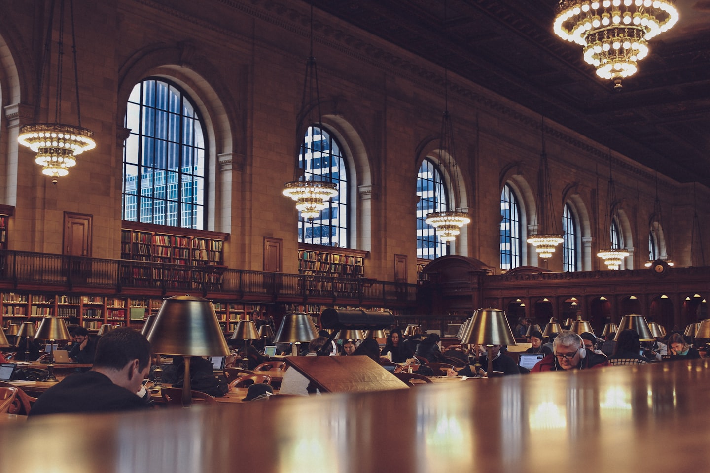 People study at long tables in a grand library reading room.