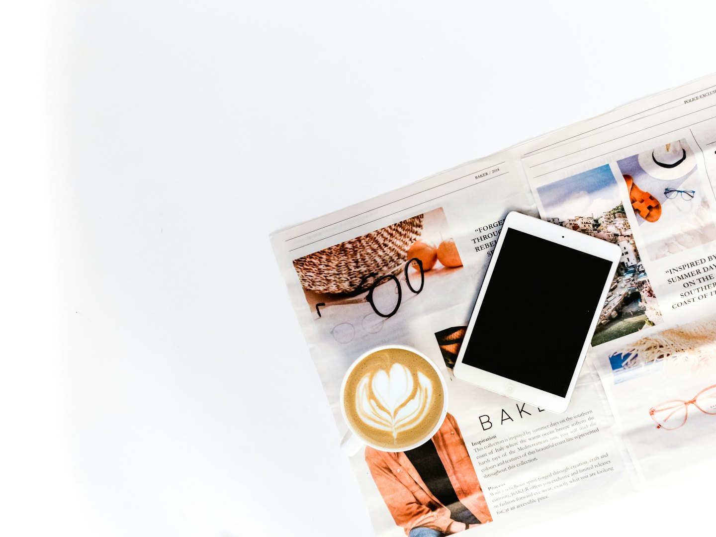 Tablet, latte with latte art, and open magazine on table.