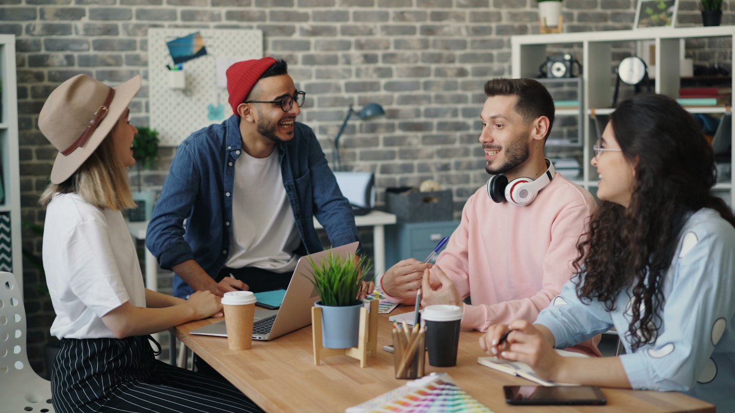 Four diverse professionals happily collaborating around an office table.