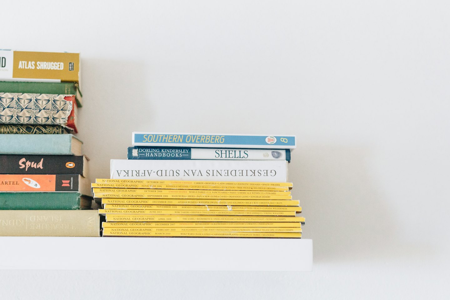 Stacks of books and National Geographic magazines on a white shelf.